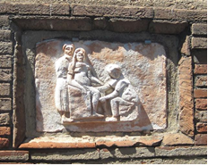 Relieve en el que se ve tres mujeres. Una sentada en la silla de parir, otra sujet&aacute;ndola y una m&aacute;s, que es la comadrona, ayudando a la mujer a parir. 